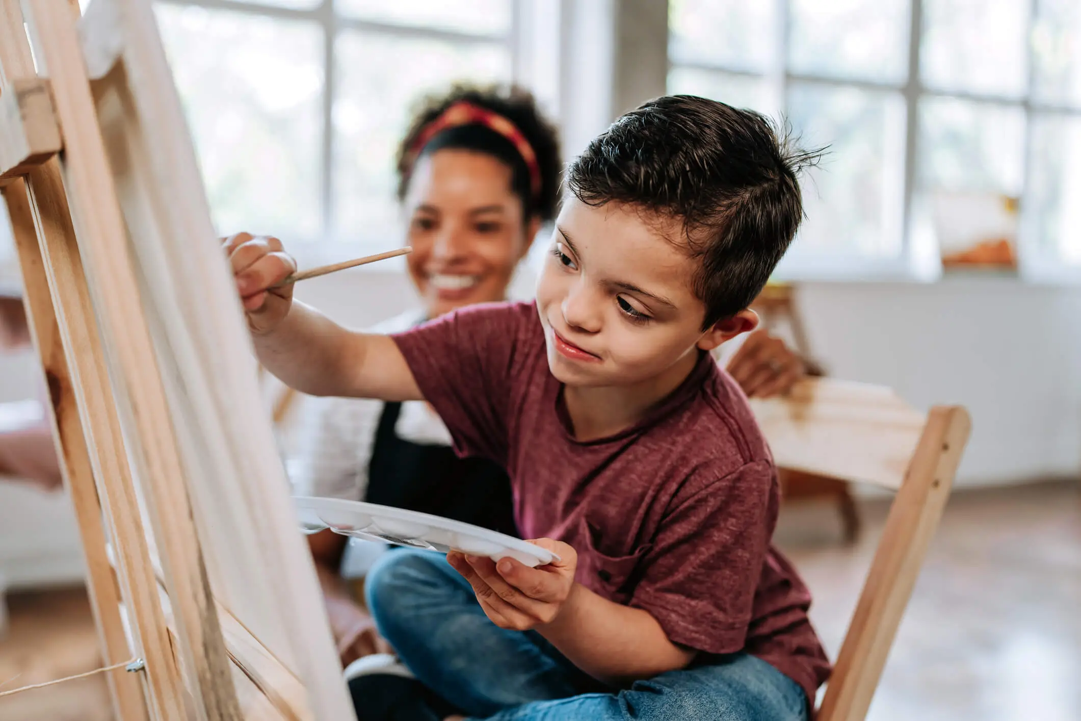 Child painting on an easel with an adult guiding nearby.