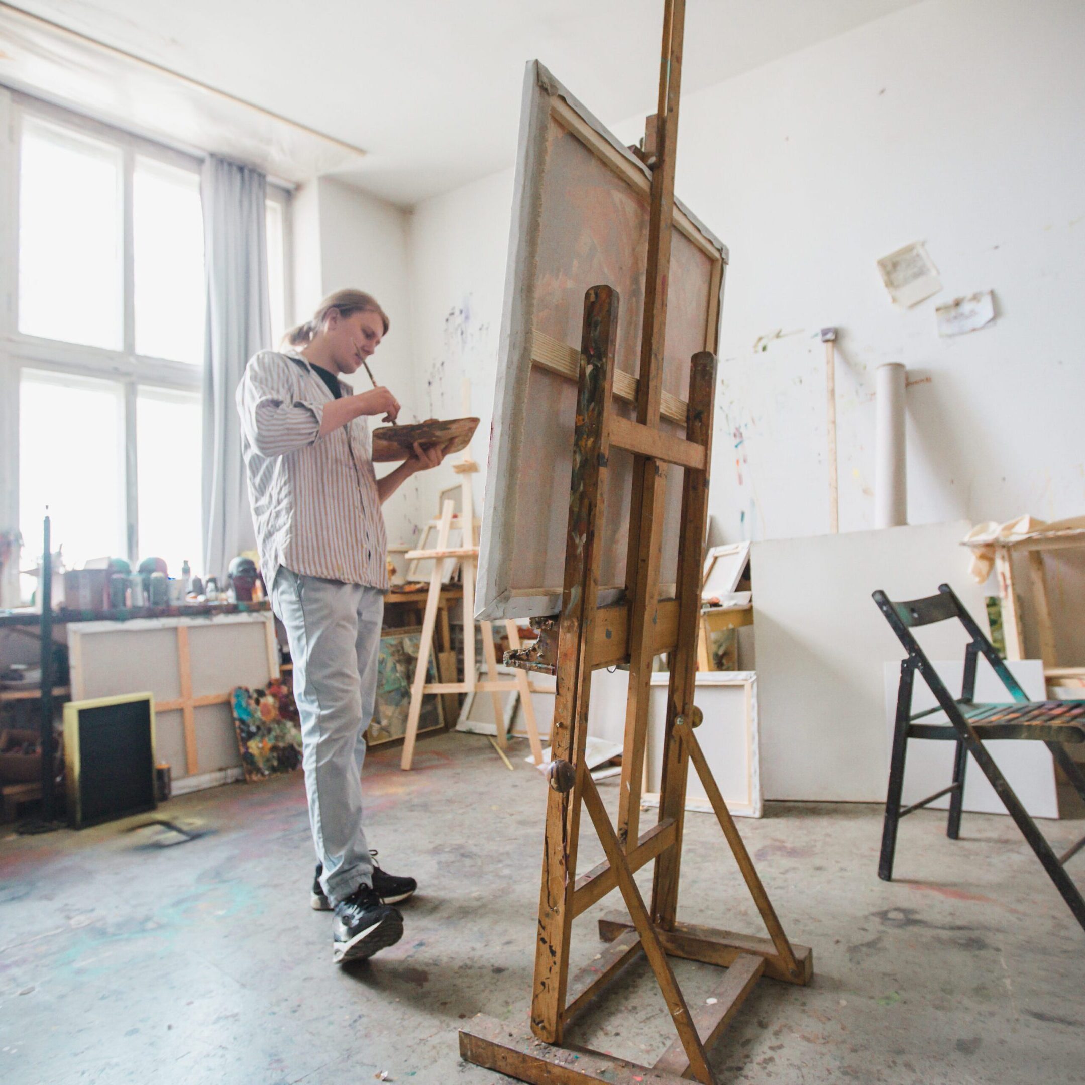 A male artist paints in his workshop against the background of the window and the staff of his instruments